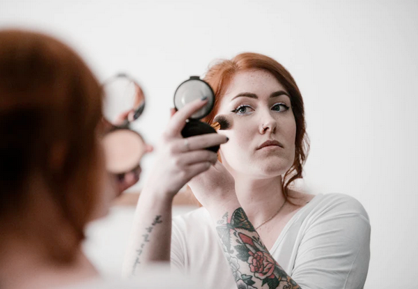 Image of a woman applying make up in a hand held mirror