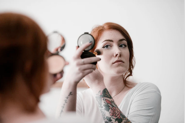 Image of a woman applying make up in a hand held mirror