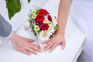 Close up of bride and groom hands during a wedding, bouquet in the background