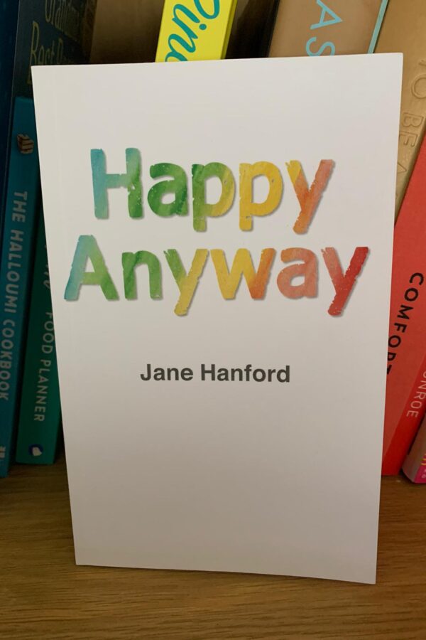 Colour image of the a white book with the words Happy Anyway in a rainbow font and the name Jane Hanford in black type
