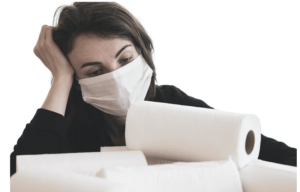 Girl wearing a face-covering over her mouth, nose and chin, looking fed up. A pile of kitchen rolls are in front of her